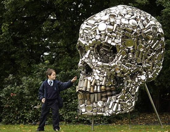 A boy standing next to a large skull made of metal.