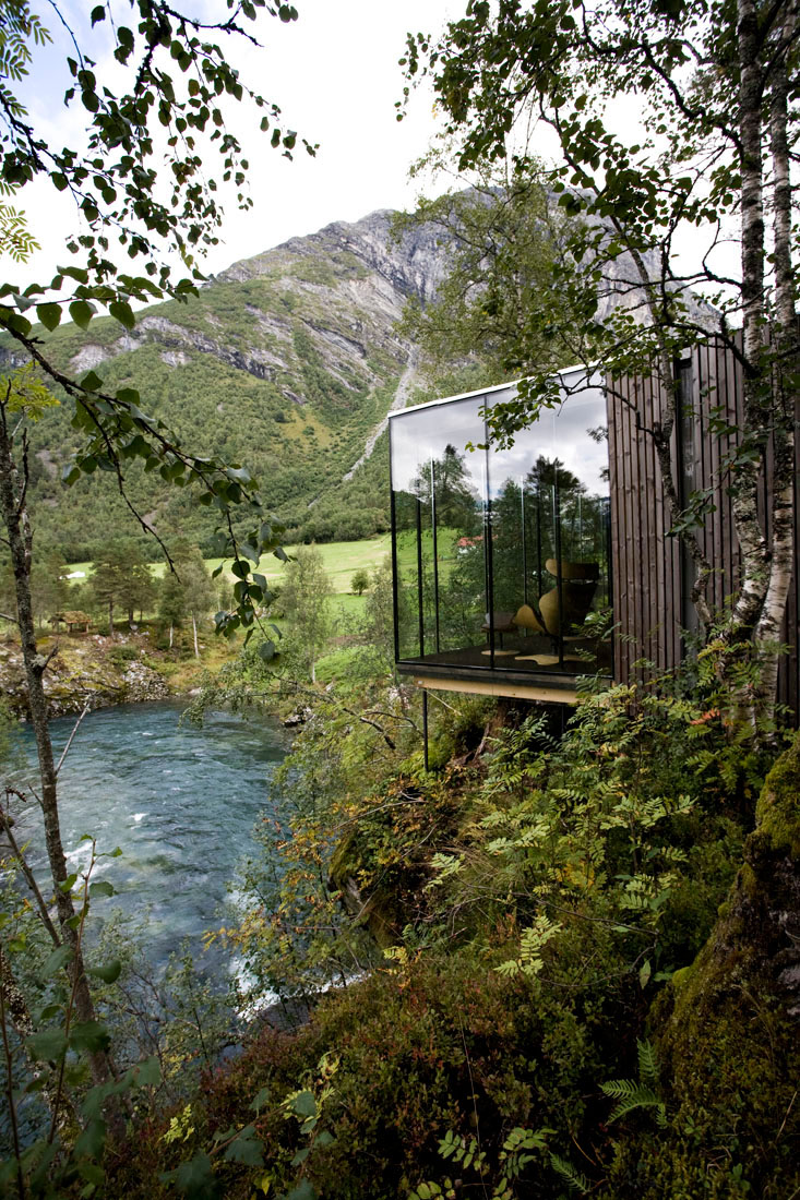 A glass building on a cliff above a river.