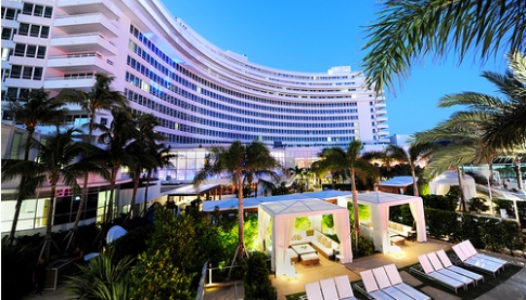 A hotel in miami at dusk with lounge chairs and palm trees.