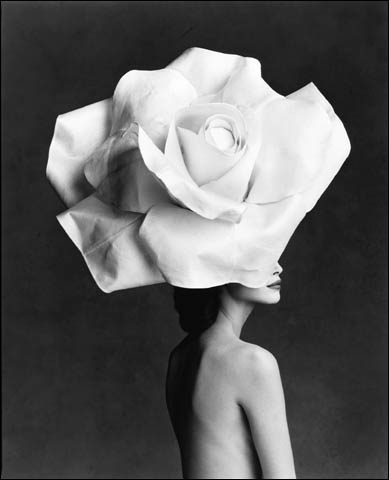 A black and white photo of a woman wearing a paper rose hat.