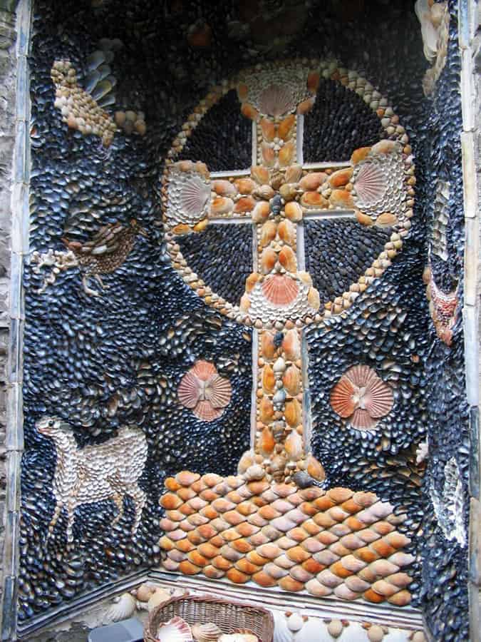 A shell art wall with a celtic cross and animals on it. Garden Folly