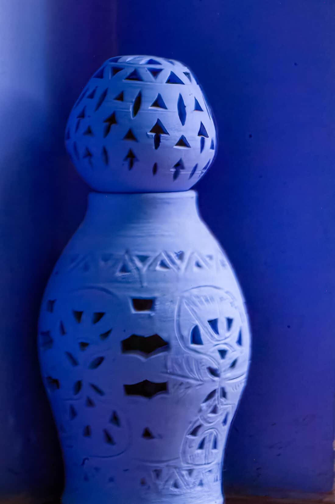 A blue ceramic vase with intricate cut-out patterns against a Majorelle Garden-inspired background.