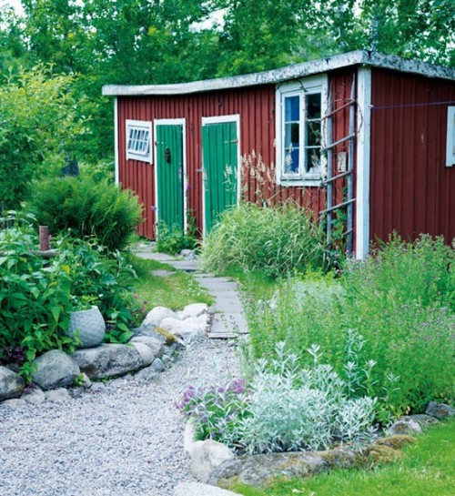 A red shed in a garden surrounded by rocks and plants.