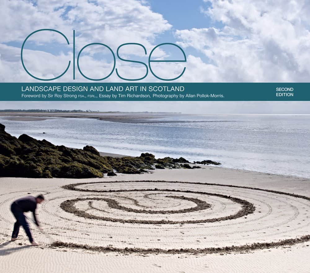 On a rocky beach with a calm sea, someone crafts a circular design in the sand. The cover reads "Close: Landscape Design and Land Art in Scotland, Second Edition" by acclaimed author Allan Pollok-Morris.