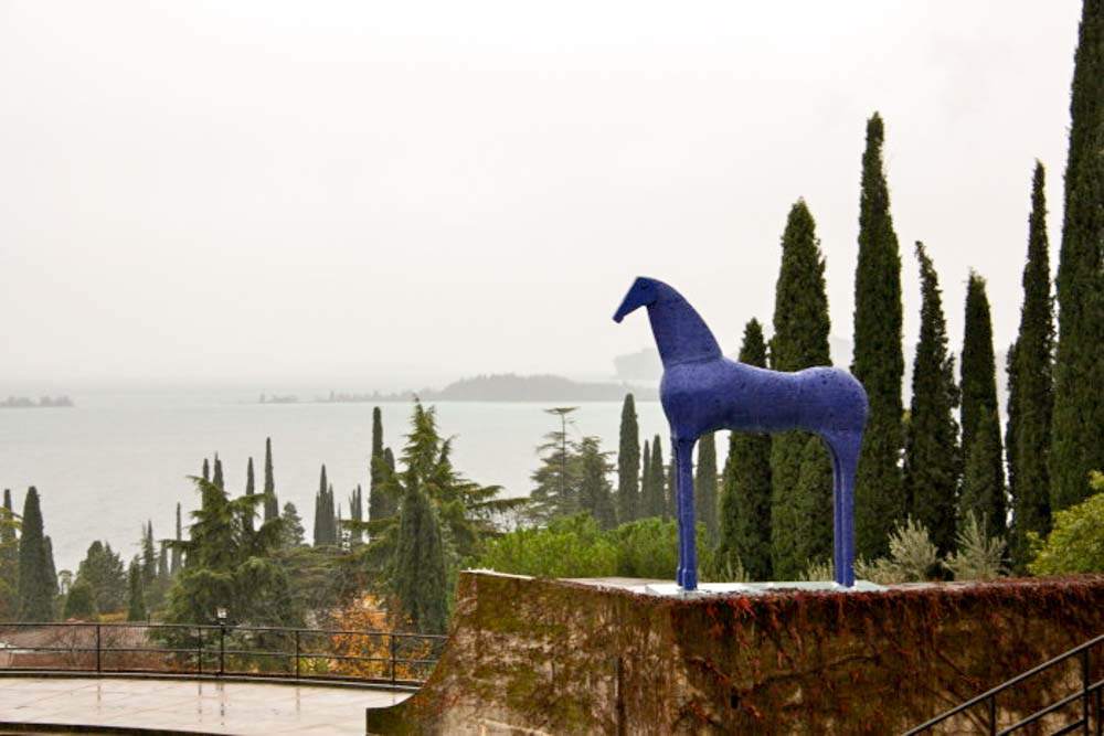 A blue statue of a horse in front of cypress trees.