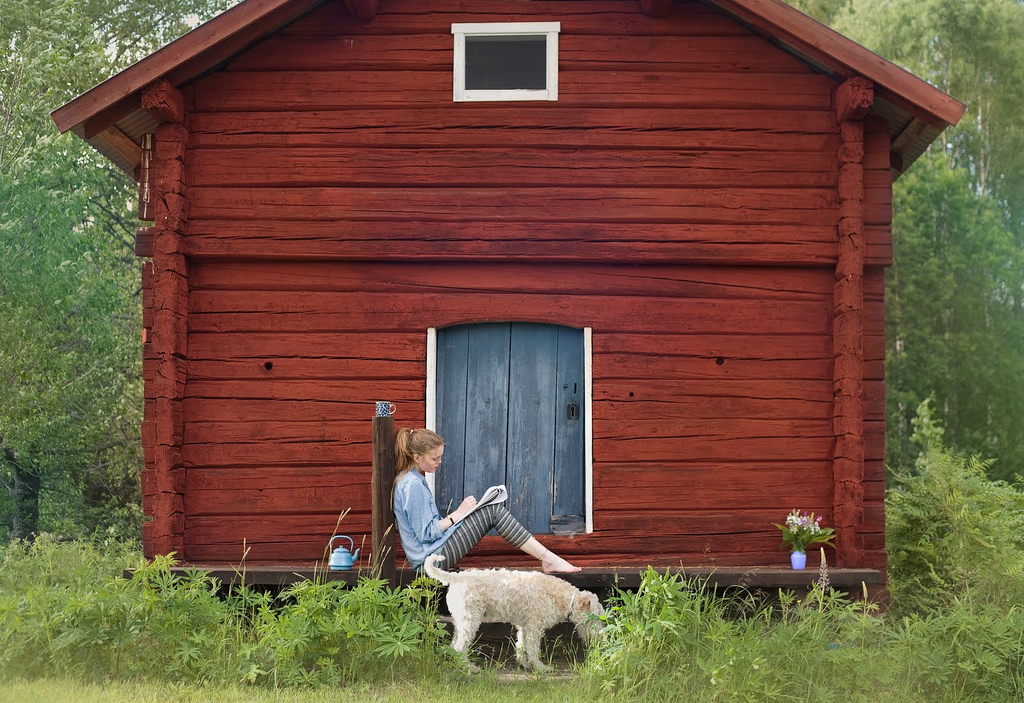 A woman sits on the porch of a red house with a dog.