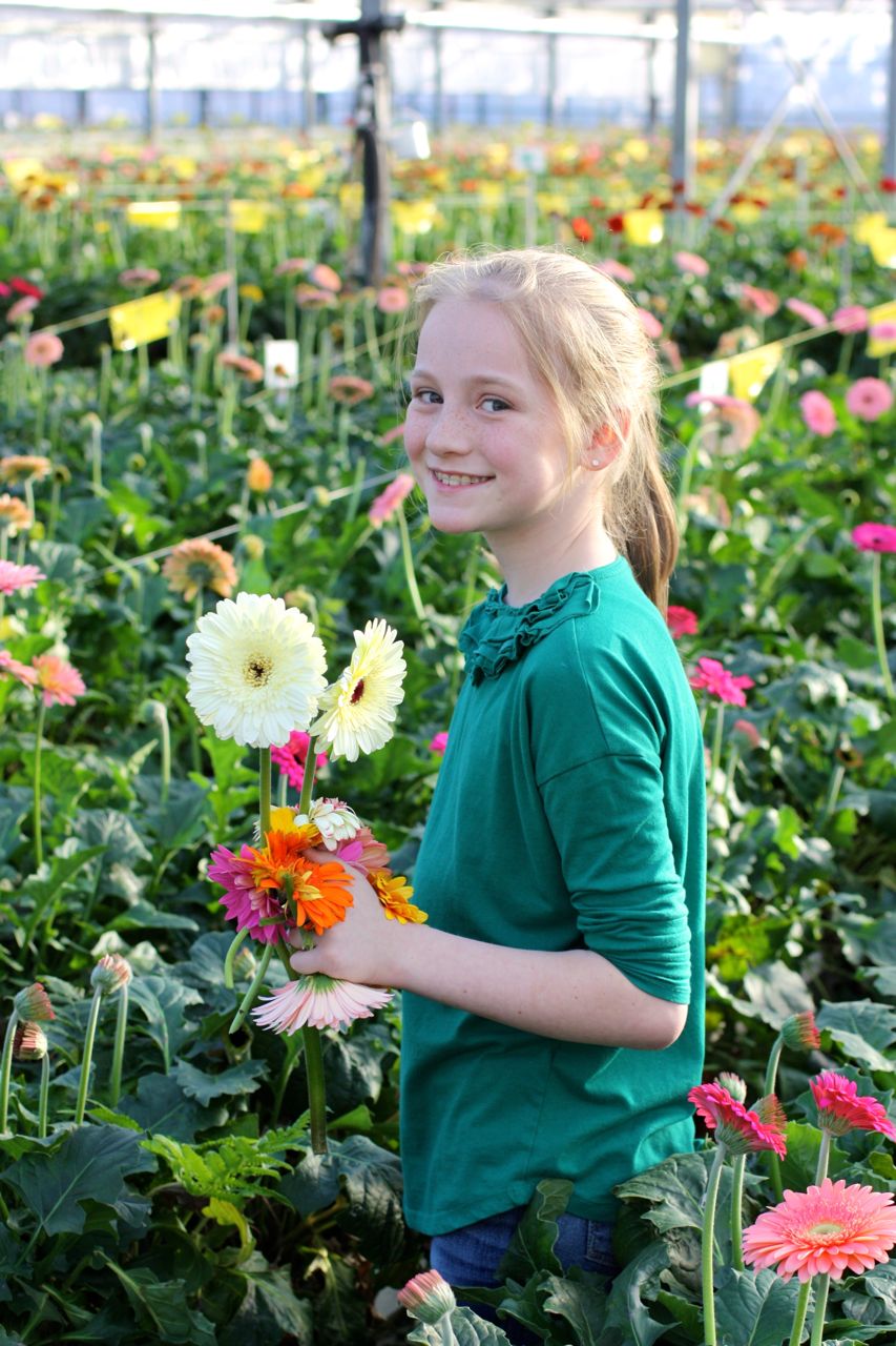 A girl conducting science fair projects in a greenhouse while holding flowers.