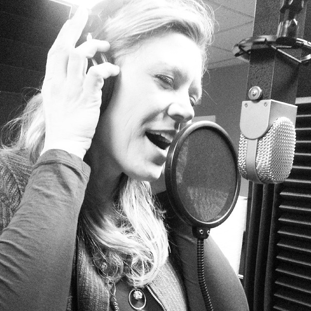 A woman singing into a microphone in a recording studio.