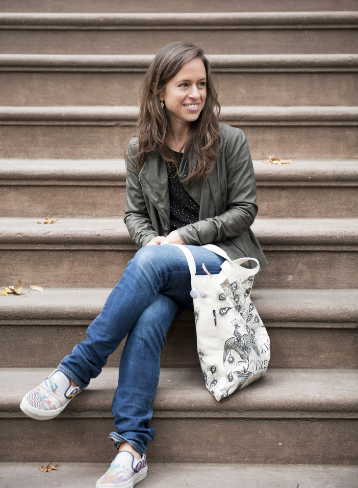 Samantha Dion Baker, an artist and author, gracefully poses on some steps with her beloved tote bag.