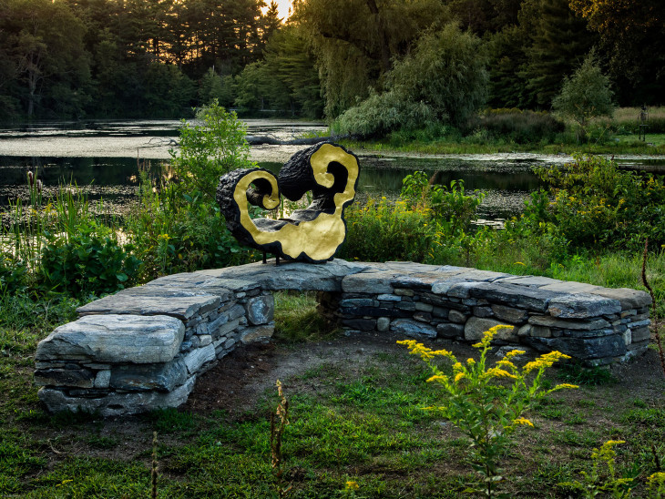 A stone bench in front of a serene pond, blending agriculture and art.
