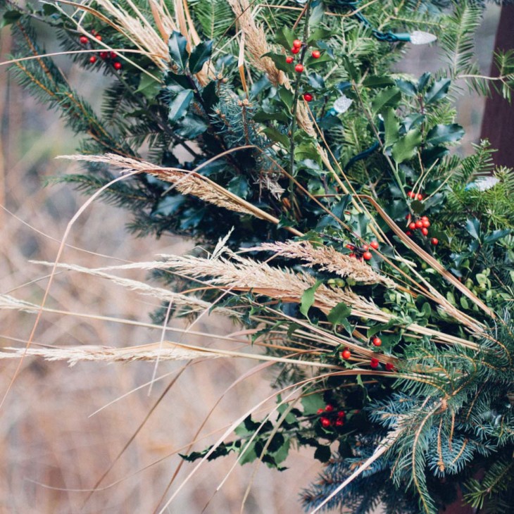 Grasses contrast with the darker foliage of the holly and evergreens giving some visual relief to a holiday wreath.