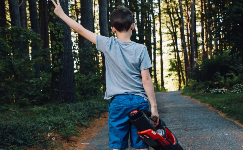 A young boy wielding a handheld blower in the woods.