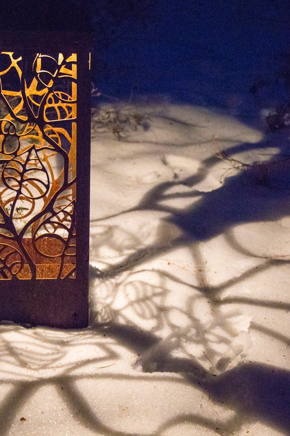 Cut metal garden light by RMI studios paints shadow images on the snow in the winter garden