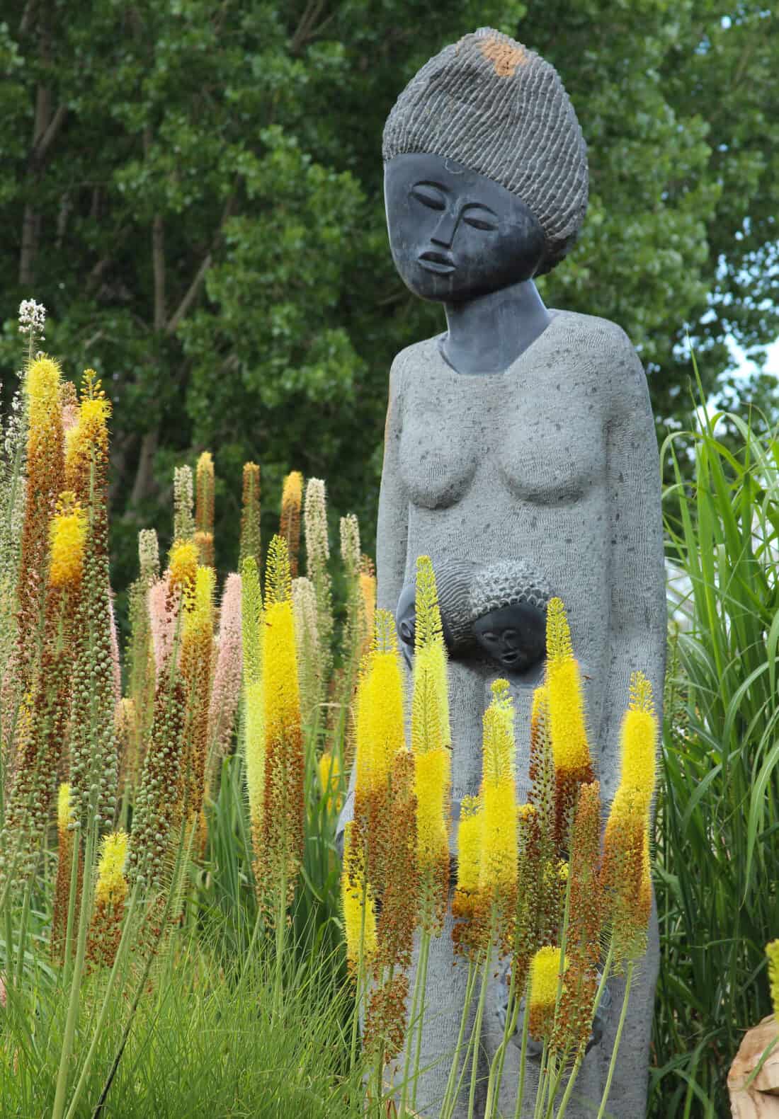 A sculpture of mother and child overlooks a bed of Foxtail Lilies 