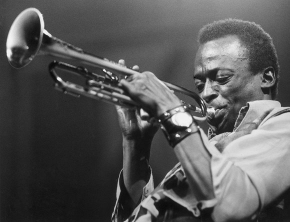 miles davis A black and white photo of a man playing a trumpet with a blue shadow.