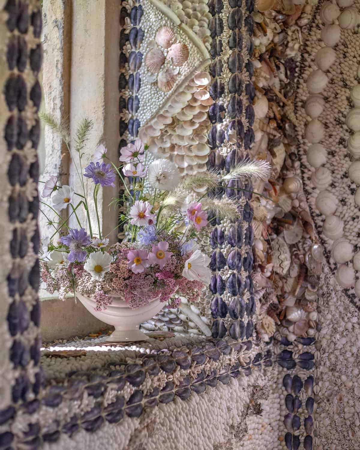 A bowl of flowers sits on a window sill in a shell house garden folly.