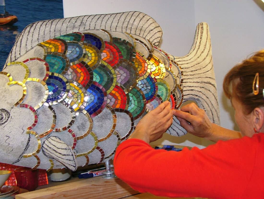 A woman working on a mosaic fish sculpture.