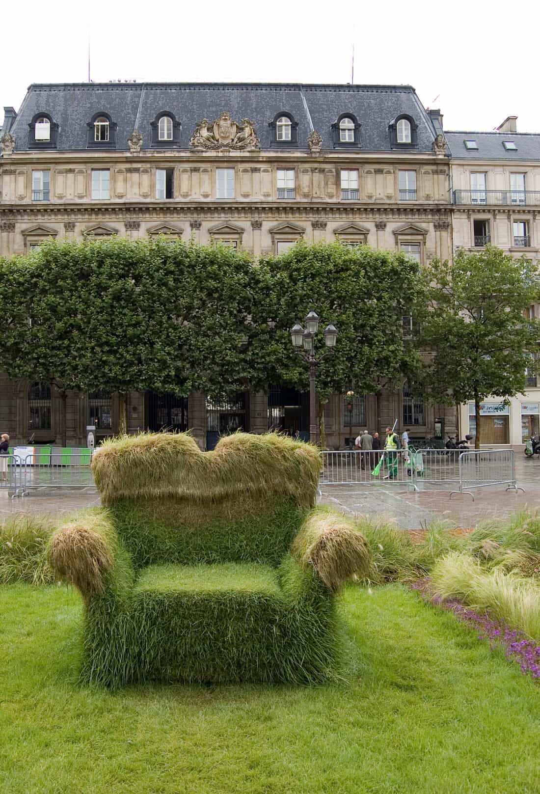 A chair made of grass in front of a building.