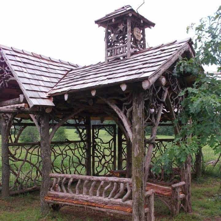 A wooden gazebo with benches in the middle of a field. by hoppy quick.