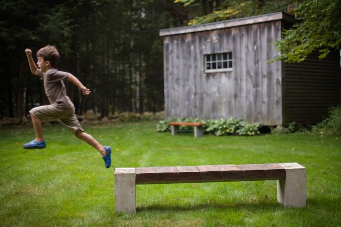 A young boy jumping over a wooden bench.
