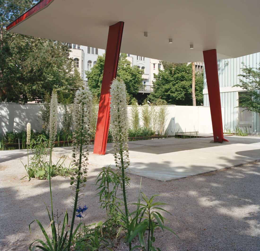 A red and white building stands in a garden that was formerly a gas station. 