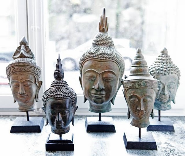 Five buddha heads on stands in front of a window.