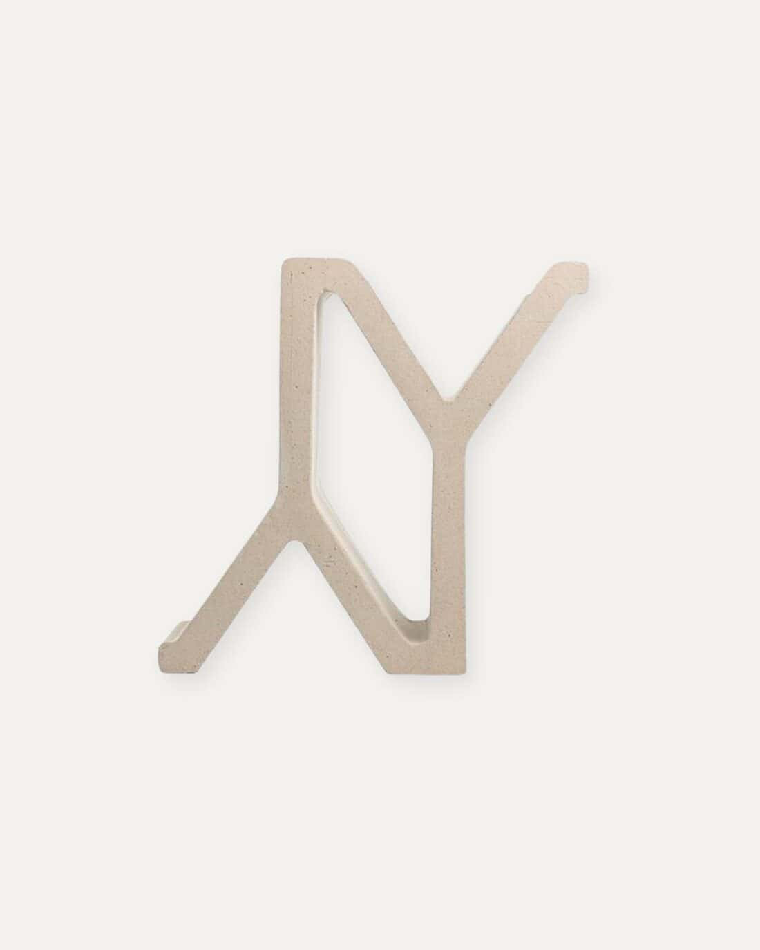 A metal letter y hanging on a white background.  Breeze block by arthur casas.