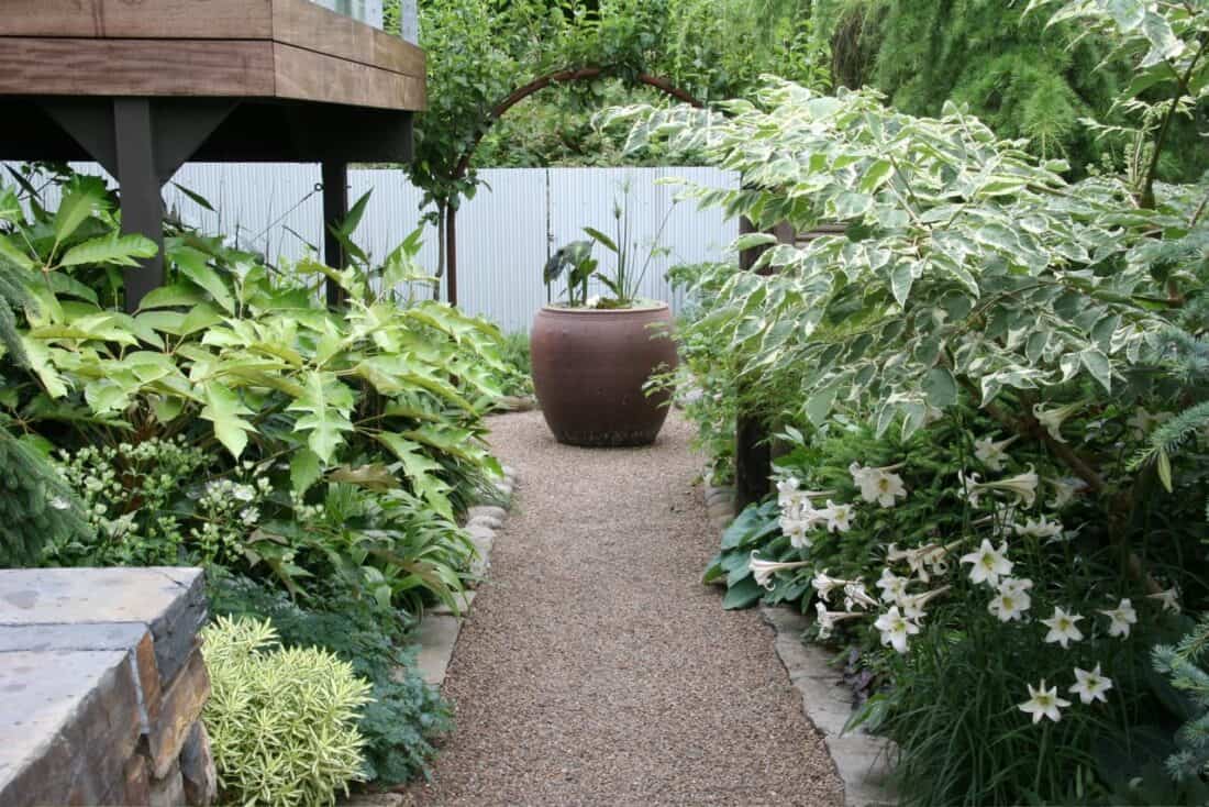 A serene garden pathway bordered by lush plants and a large decorative pot.