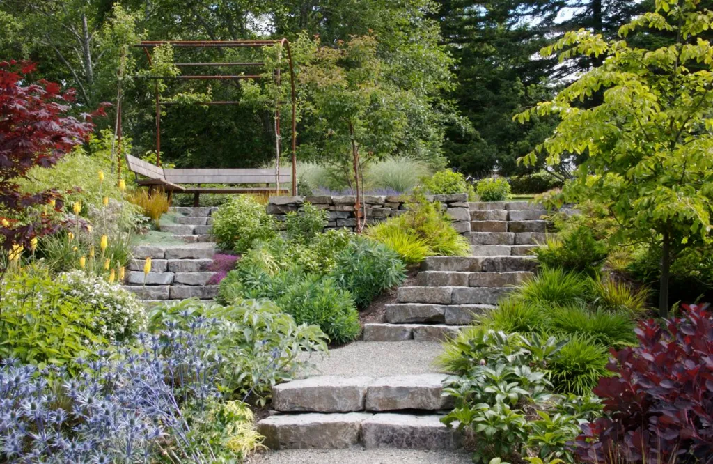 A serene garden path with stone steps flanked by lush, colorful foliage and leading to a wooden pergola.