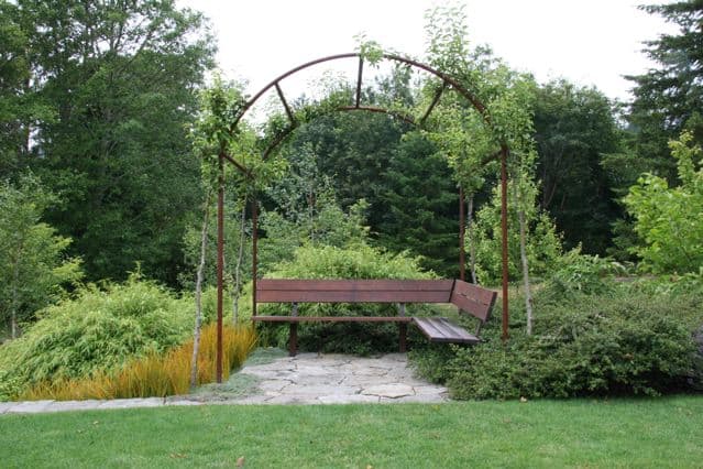 A metal garden swing with overgrown plants in a lush green setting.