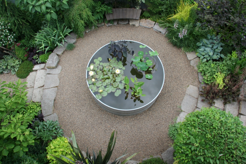 Circular garden pond surrounded by well-maintained plants and pebble paths.