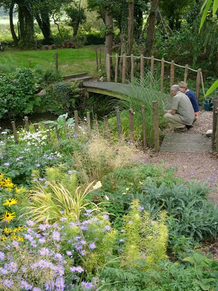 A man sits on a wooden bridge in a garden.