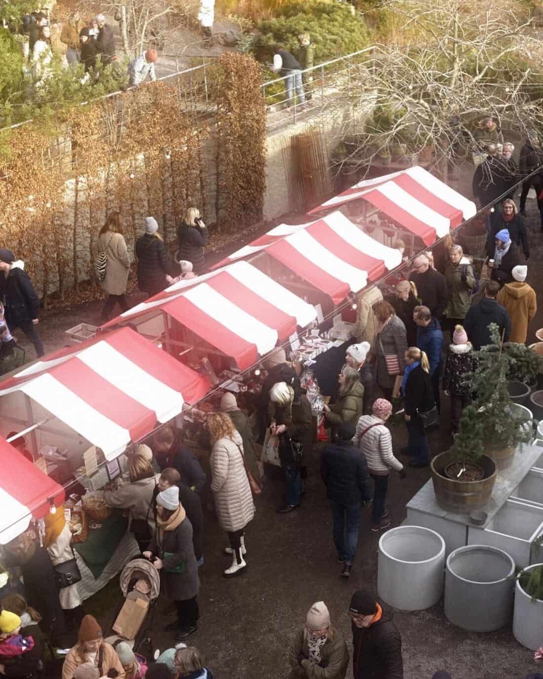Outdoor market with red-and-white striped awnings, bustling with shoppers.