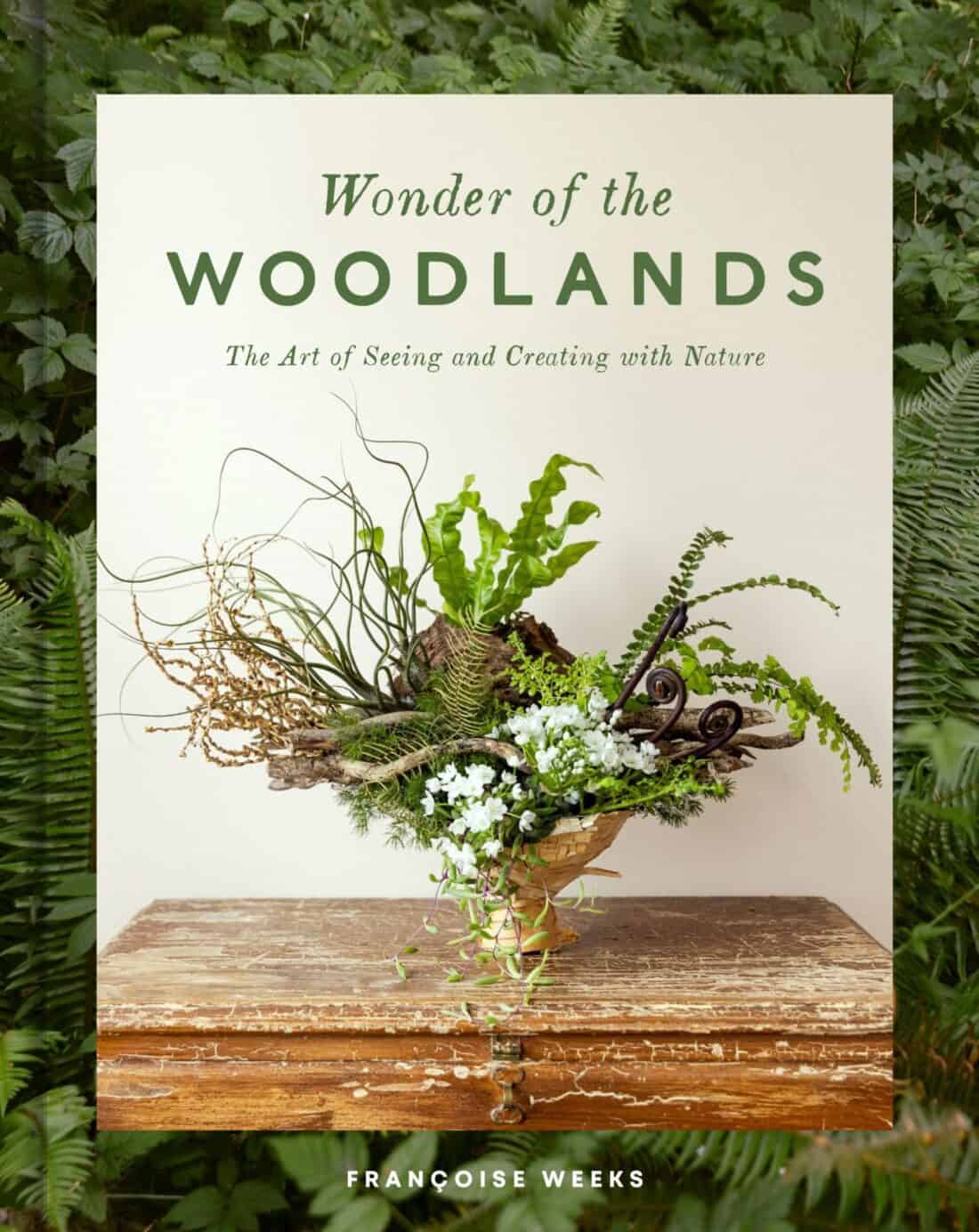 A book titled "Wonder of the Woodland Garden" by Françoise Weeks, featuring a cover with a floral arrangement on a wooden table against a greenery backdrop.