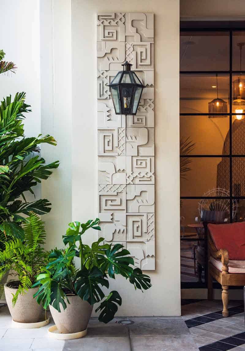 Elegant entrance with lantern hanging beside a decorative carved white panel, flanked by potted plants.