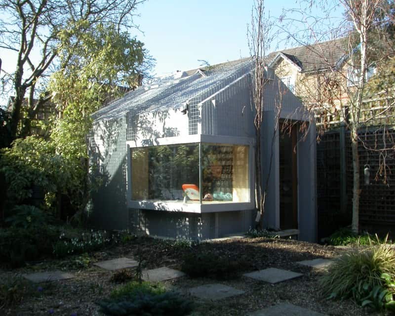 A modern extension with large glass windows on a traditional brick house, overlooking a garden.