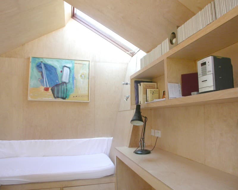 Compact wooden interior of a small living space with a single bed, desk, and shelves.