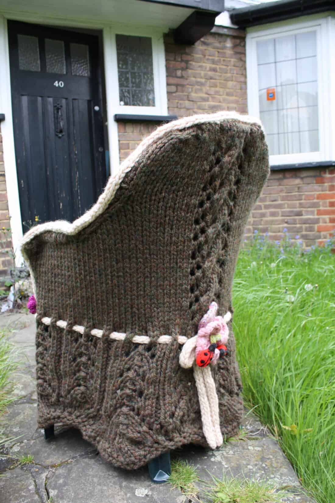 A knitted cozy covering a wingback chair outside a brick house.