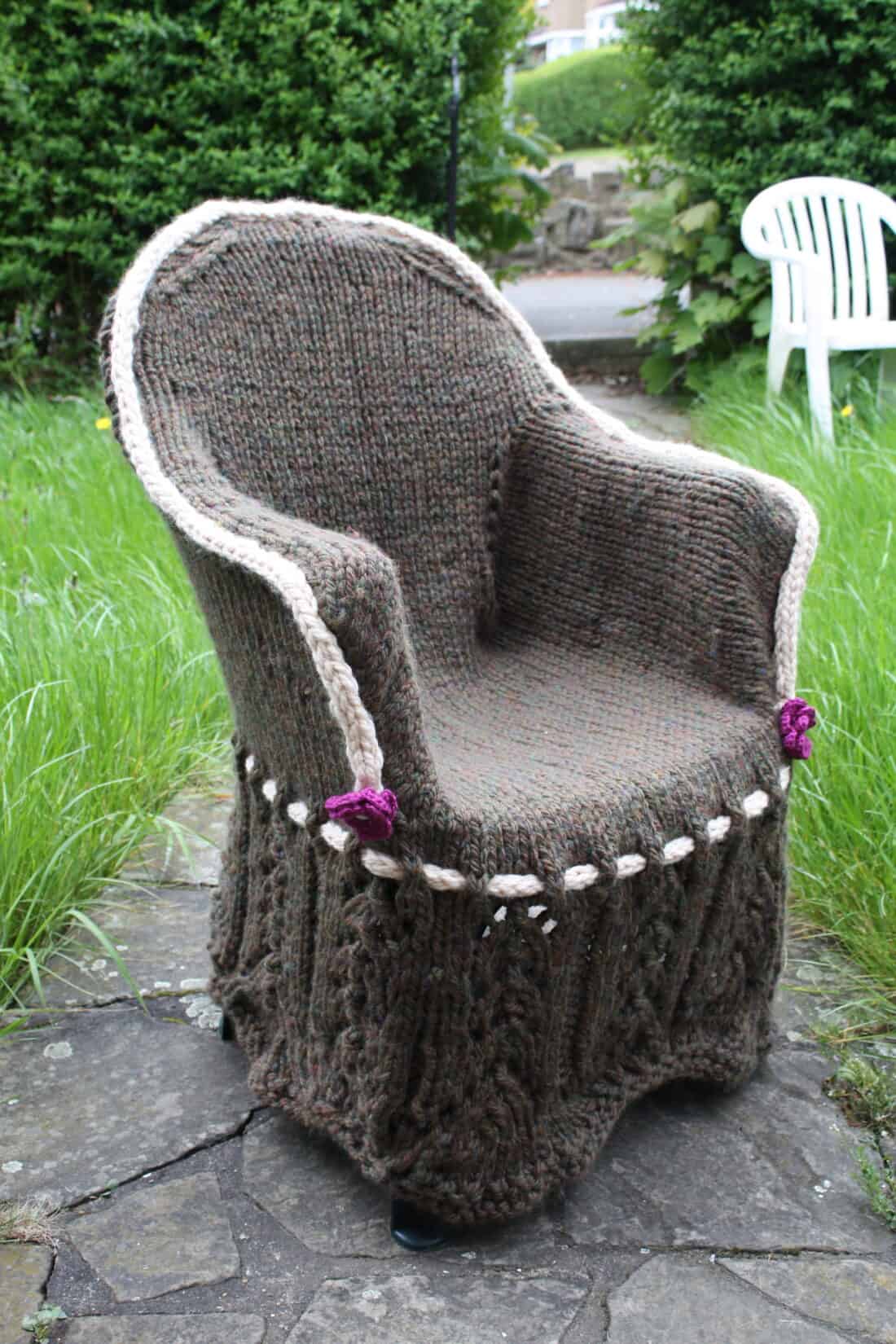 Knitted cover on an outdoor chair adorned with flowers and decorative trim.