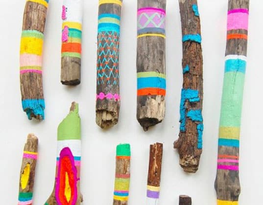 Assorted wooden sticks, crafted from driftwood and painted with bright, colorful patterns including stripes, zigzags, and geometric shapes, arranged on a white background. Perfect for various garden uses or art projects.